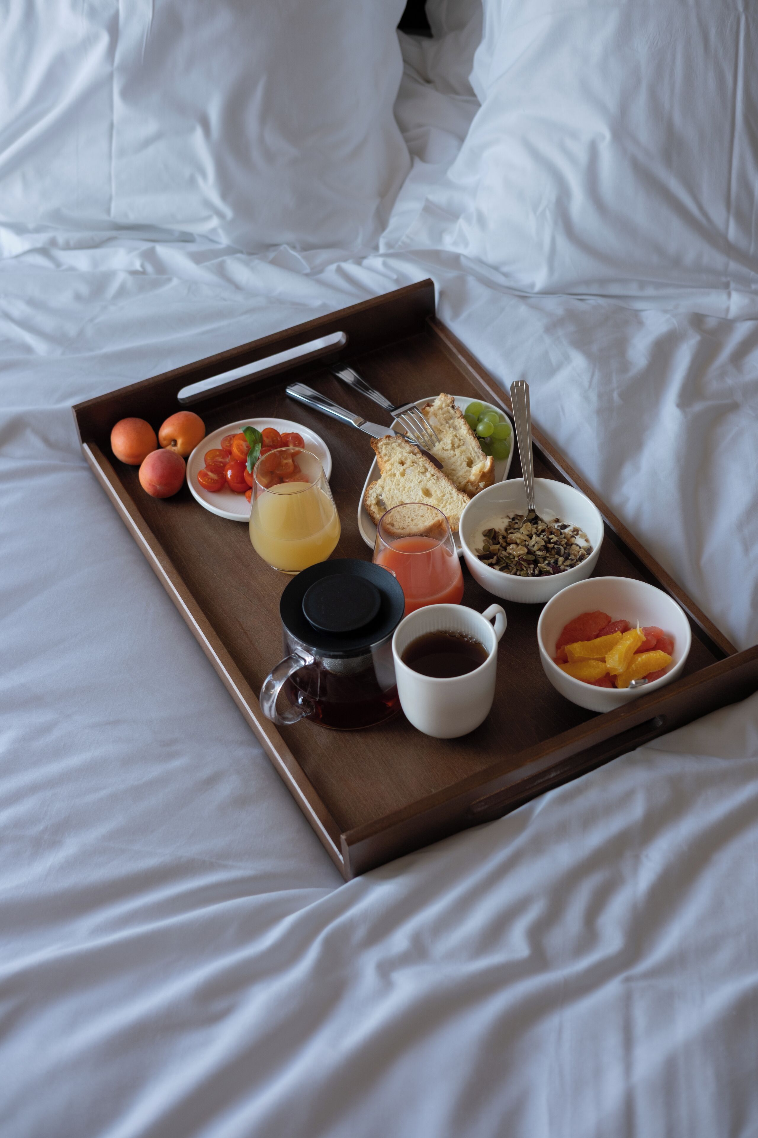Ontbijtplateau met fruit, toast, ontbijtgranen en drankjes op een bed.