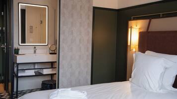 Hotelkamer met een bed, nachtkastje, spiegel, wandlamp en badkamer met wastafel en handdoekhouder.