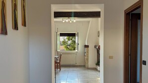 Un passadís amb sòl de rajola, una finestra amb vista a vegetació, un radiador i una porta a la dreta.