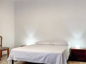 A bedroom with a bed, a chair, and a nightstand with a lamp.
