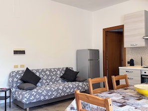 A compact living space with a sofa, a dining table, chairs, a refrigerator, and a kitchen area.