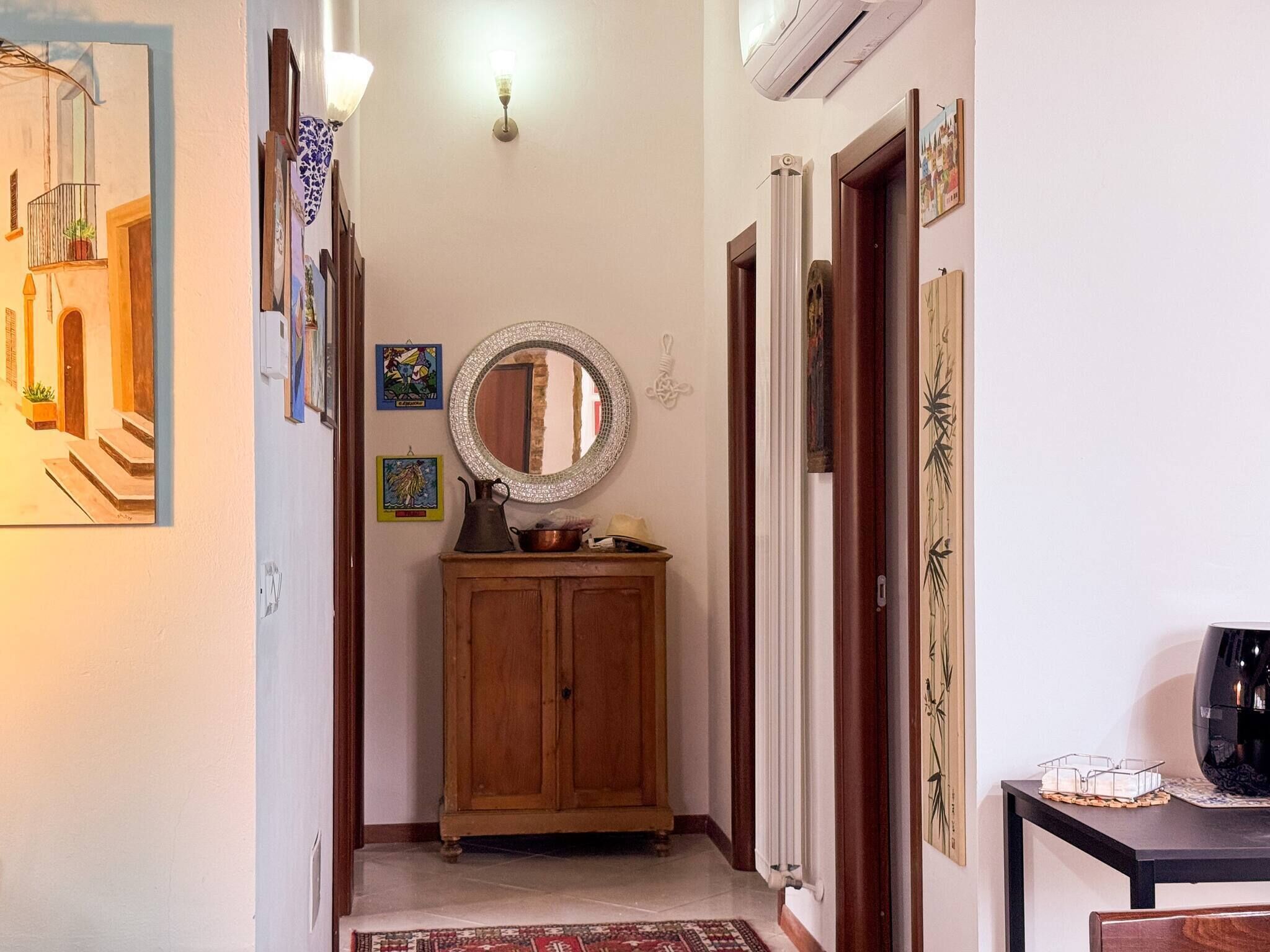 A hallway with a wooden cabinet, a mirror, wall-mounted artwork, and a radiator.