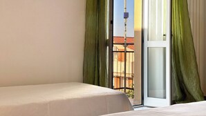 A hotel room with a bed, a sliding glass door to the outside, and a view of buildings and a tower.