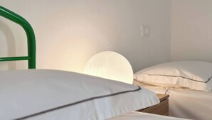 A simple, clean room with a single bed, a bedside table, and a wall-mounted light.