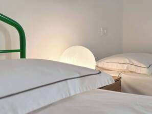 A simple, clean room with a single bed, a bedside table, and a wall-mounted light.