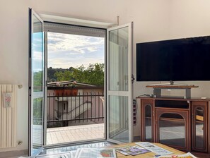 A room with a sliding glass door leading to a balcony, a flat-screen TV, and a wooden cabinet. - Mare, Monti e Limoni (Marina di San Vito)