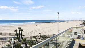 Une vue sur la plage depuis un balcon, avec des palmiers, un ciel dégagé et une côte lointaine.