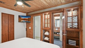 Une chambre avec un grand lit, une armoire en bois, un tableau et des étagères intégrées où sont rangées des serviettes.