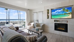 Un salon moderne avec une cheminée, un canapé en cuir et un grand écran de télévision diffusant une scène de plage.