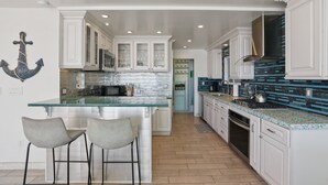 Une cuisine moderne avec des meubles blancs, un îlot central en verre et un dosseret de cuisine recouvert de carreaux bleus.