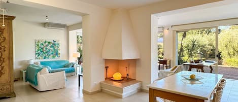 A modern living room with a fireplace, a dining area with a table and chairs, and a view of the outdoors.