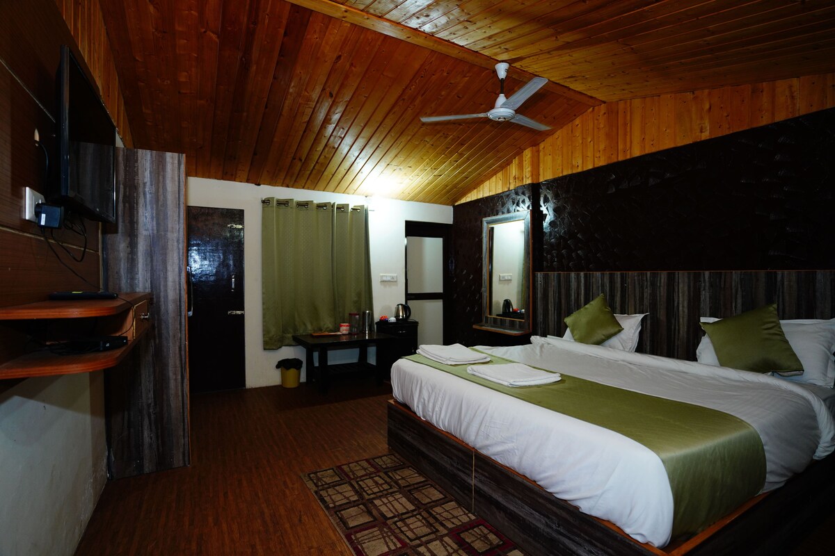 Ein Schlafzimmer mit Holzbalkendecke, einem Bett mit weißer Bettwäsche und grünen Kissen, einem Schreibtisch mit Computer und einem Spiegel an der Wand.