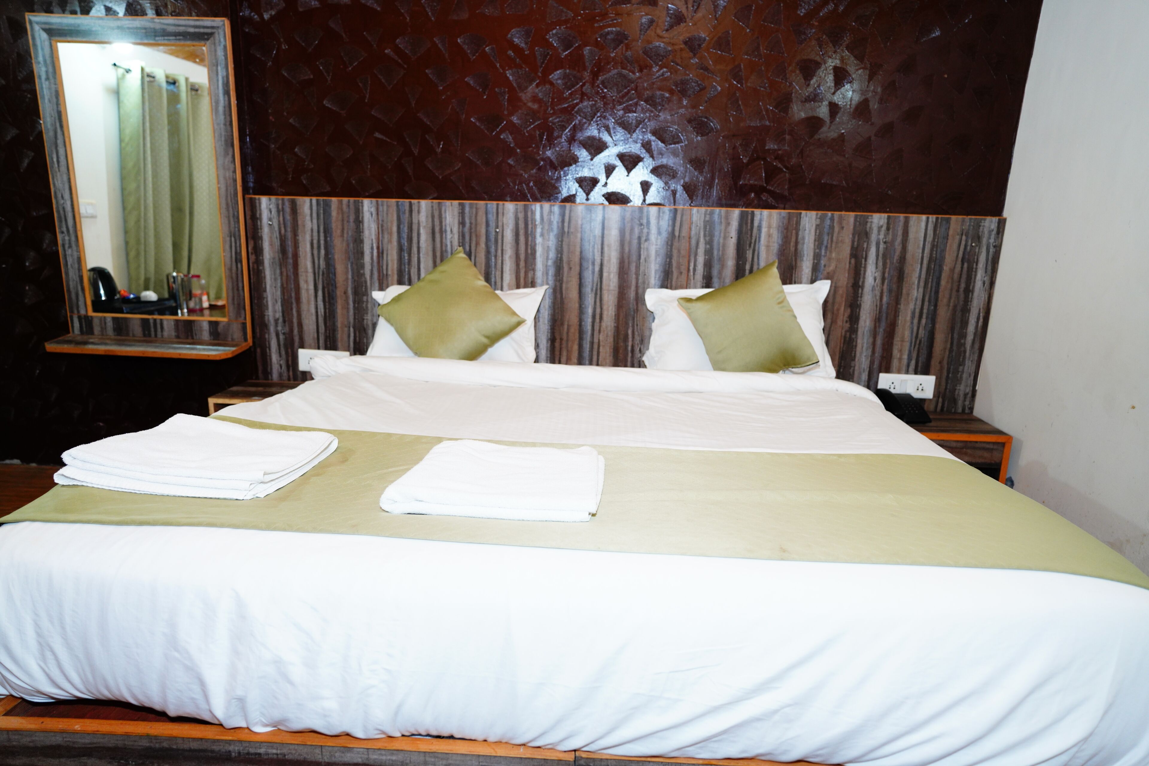 A neatly made bed with white linens and two green pillows, a wooden headboard, and a mirror on the wall.