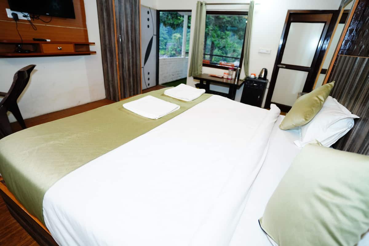 A hotel room with a bed, a desk, a chair, a TV, and a window with a view of greenery.