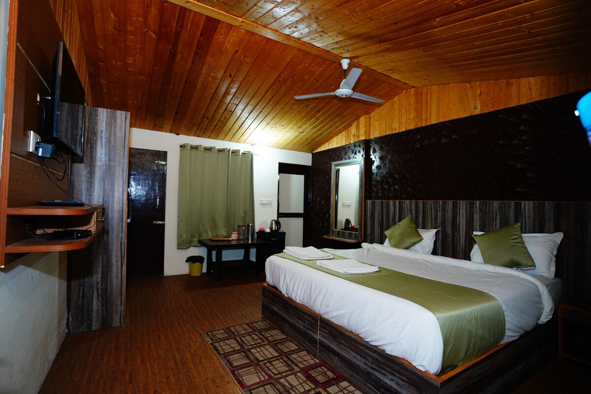 A wooden-paneled bedroom with a bed, a ceiling fan, a TV, and a small table with a lamp.