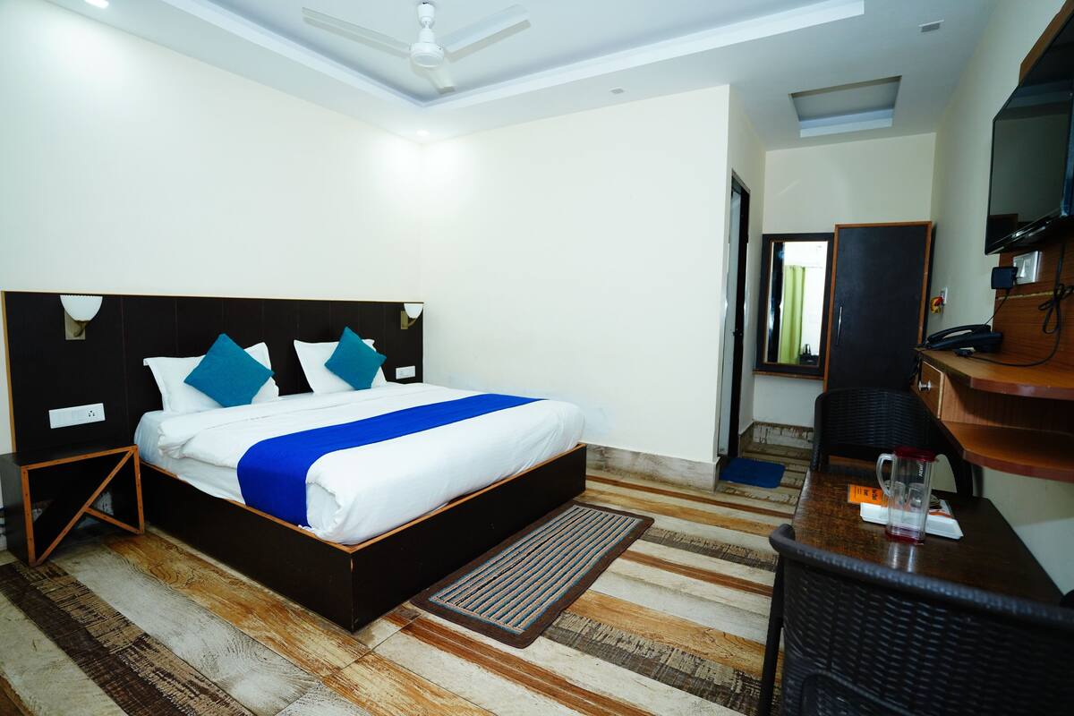 A hotel room with a bed, a desk, a chair, a television, and a window.
