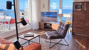 A modern living room with a large TV, comfortable seating, a wooden cabinet, and a view of the sea. - Penthouse Olpenitz Living - Sea View, Sauna, Elevator, Underground Parking Space (Olpenitz)