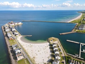 Oversigtsbillede af et kystområde med en lystbådehavn, en sandstrand og boligbygninger.