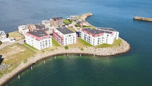 A coastal residential area with modern apartment buildings, a rocky breakwater, and a clear view of the sea. - Penthouse Olpenitz Living - Sea View, Sauna, Elevator, Underground Parking Space (Olpenitz)