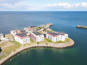 Een kustwoongebied met moderne appartementencomplexen, een rotsachtige zeewering en een helder uitzicht op de zee.