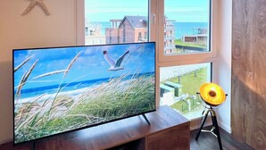 A room with a TV displaying a beach scene, a starfish decoration, and a lamp. - Penthouse Olpenitz Living - Sea View, Sauna, Elevator, Underground Parking Space (Olpenitz)