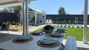 An outdoor patio with a white table set for dining, a pool, and a covered seating area in the background. - Eastport - Luxury Beach Retreat with Plunge Pool (Catherine Hill Bay)