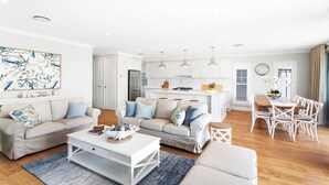 A modern living room with a sofa set, a coffee table, and a dining area with a wooden table and chairs. - Eastport - Luxury Beach Retreat with Plunge Pool (Catherine Hill Bay)