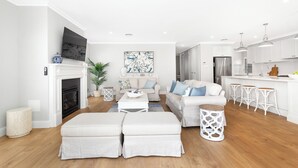 A modern living room with a fireplace, sofas, a coffee table, and a kitchen area with bar stools. - Eastport - Luxury Beach Retreat with Plunge Pool (Catherine Hill Bay)