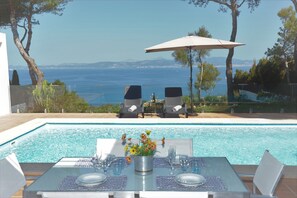 Relax by the sea with a poolside dining area, complete with a table, lounge chairs, and lush surroundings.