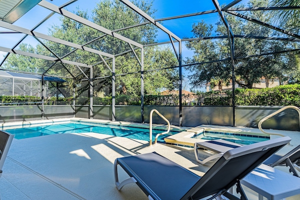 This beautiful southwest-facing pool area features a large private swimming pool, a relaxing spillover spa, multiple sun loungers, and a fully screened enclosure for added privacy and comfort.