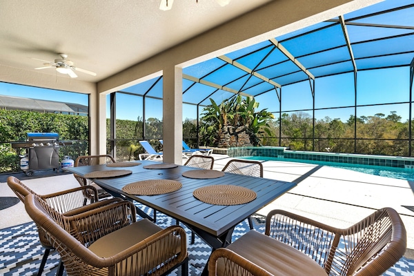 This covered outdoor space features a large dining table with seating for six, stylish wicker chairs, a ceiling fan for added comfort, and direct views of the screened-in pool, and spa.