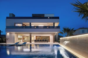 Une maison moderne à deux étages dotée d’une piscine, de mobilier d’extérieur et d’une cascade décorative.