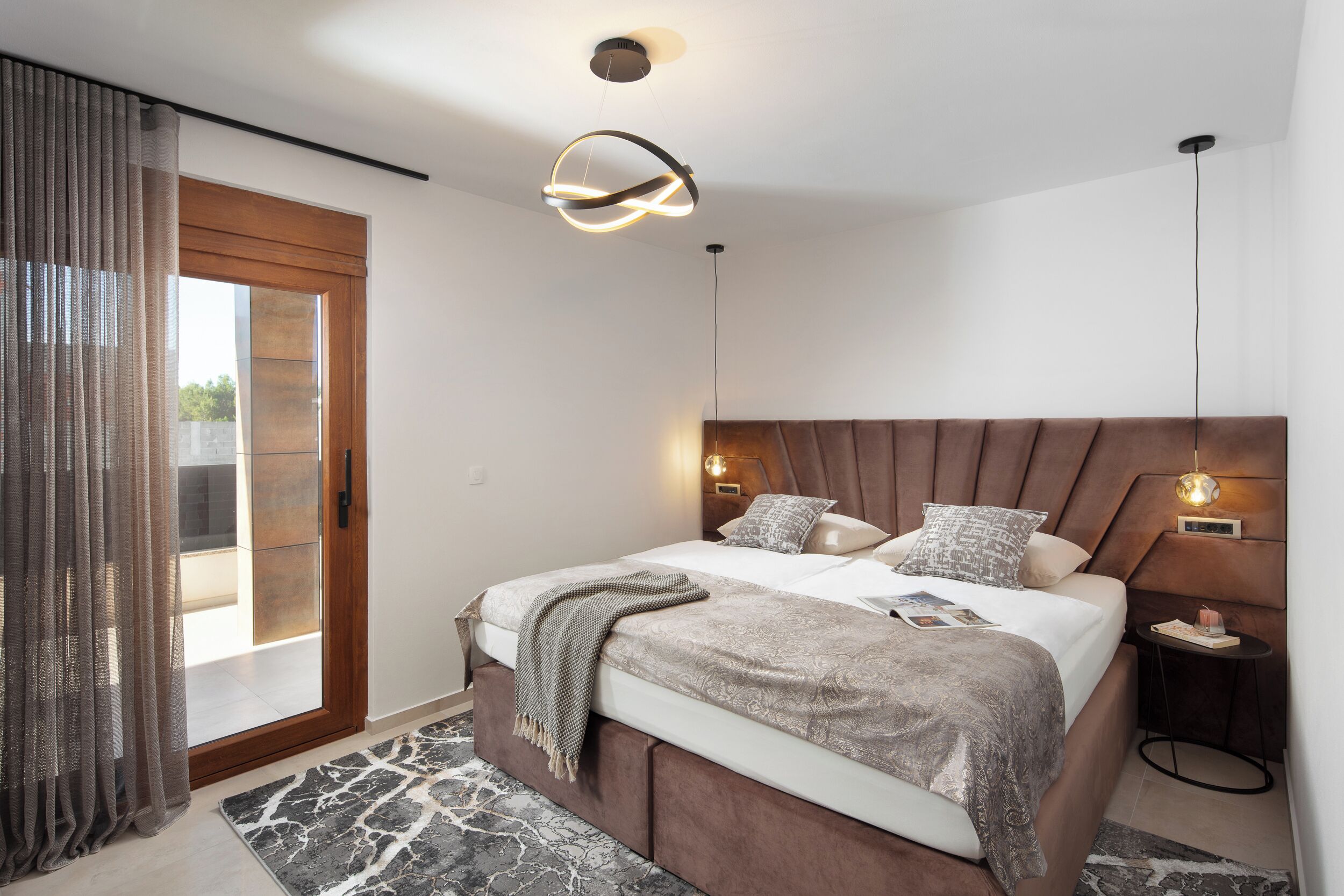 A modern bedroom with a large bed, a wooden headboard, two bedside tables, and a view through a glass door.
