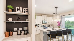 A modern kitchen with white cabinetry, a coffee station, and a dining area with bar stools.