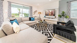 A modern living room with a sectional sofa, a black armchair, a coffee table, and a TV mounted on the wall.