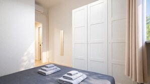Quarto com cama, duas toalhas dobradas, guarda-roupa e janela com cortinas.