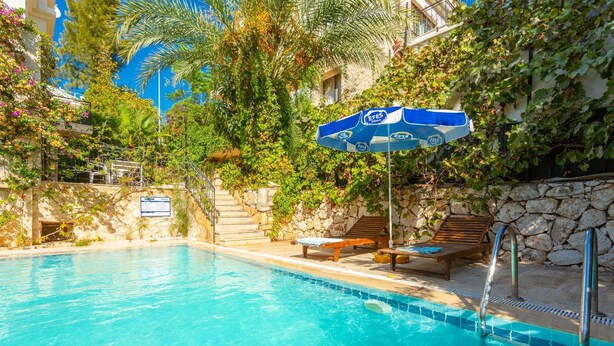 A swimming pool with a stone wall, wooden lounge chairs, and an umbrella.