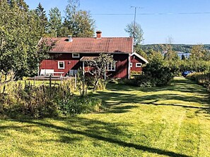 A red barn with a sloped roof, surrounded by a well-maintained grassy area and trees. - 4 Star Holiday Home in Ammeberg (Åmmeberg)
