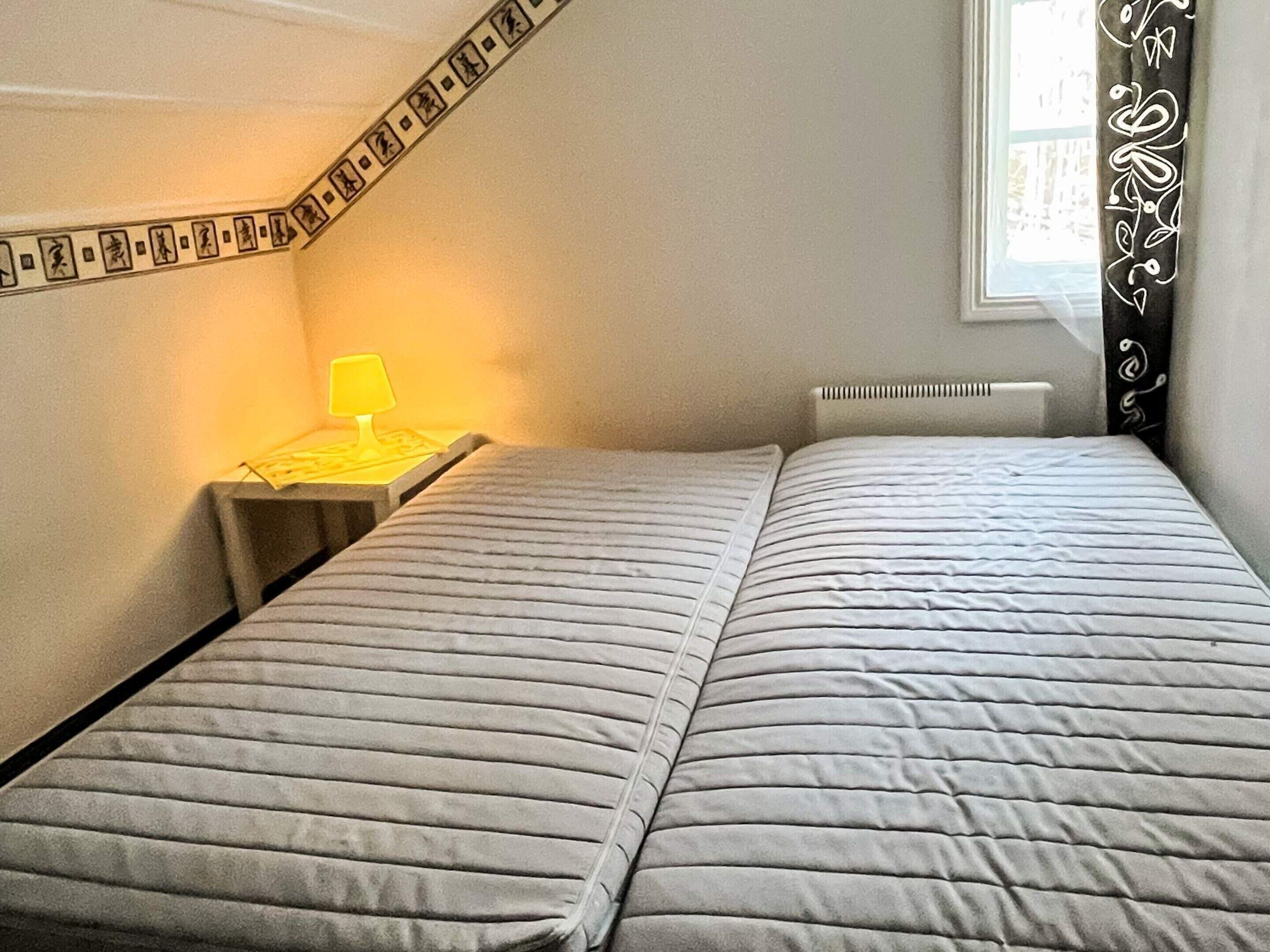 A bedroom with a bed, a nightstand, a lamp, and a window with curtains.