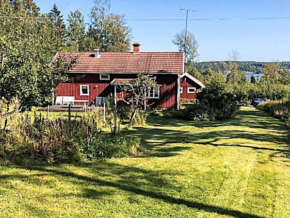 A red barn with a sloped roof, surrounded by a well-maintained lawn and trees. - 4 Star Holiday Home in Ammeberg (Åmmeberg)