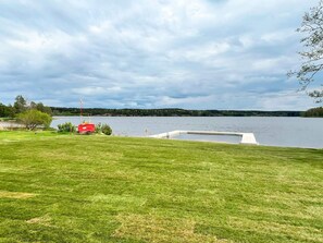 A grassy area with a dock extending into a lake, surrounded by trees and a cloudy sky. - 4 Star Holiday Home in Ammeberg (Åmmeberg)