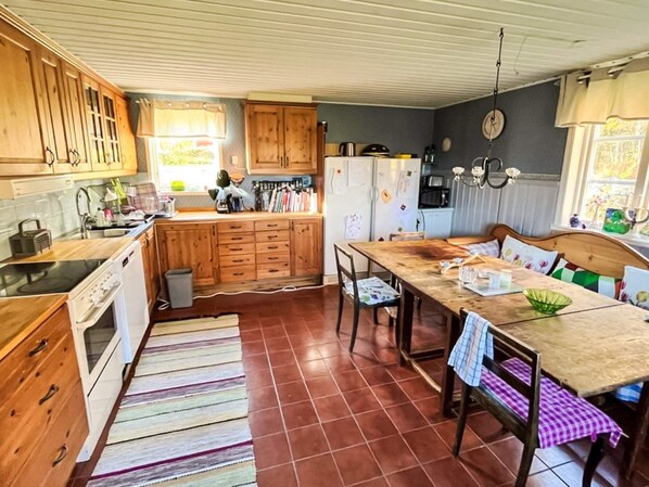 A kitchen with wooden cabinets, a stove, a refrigerator, and a dining table with chairs. - 4 Star Holiday Home in Ammeberg (Åmmeberg)