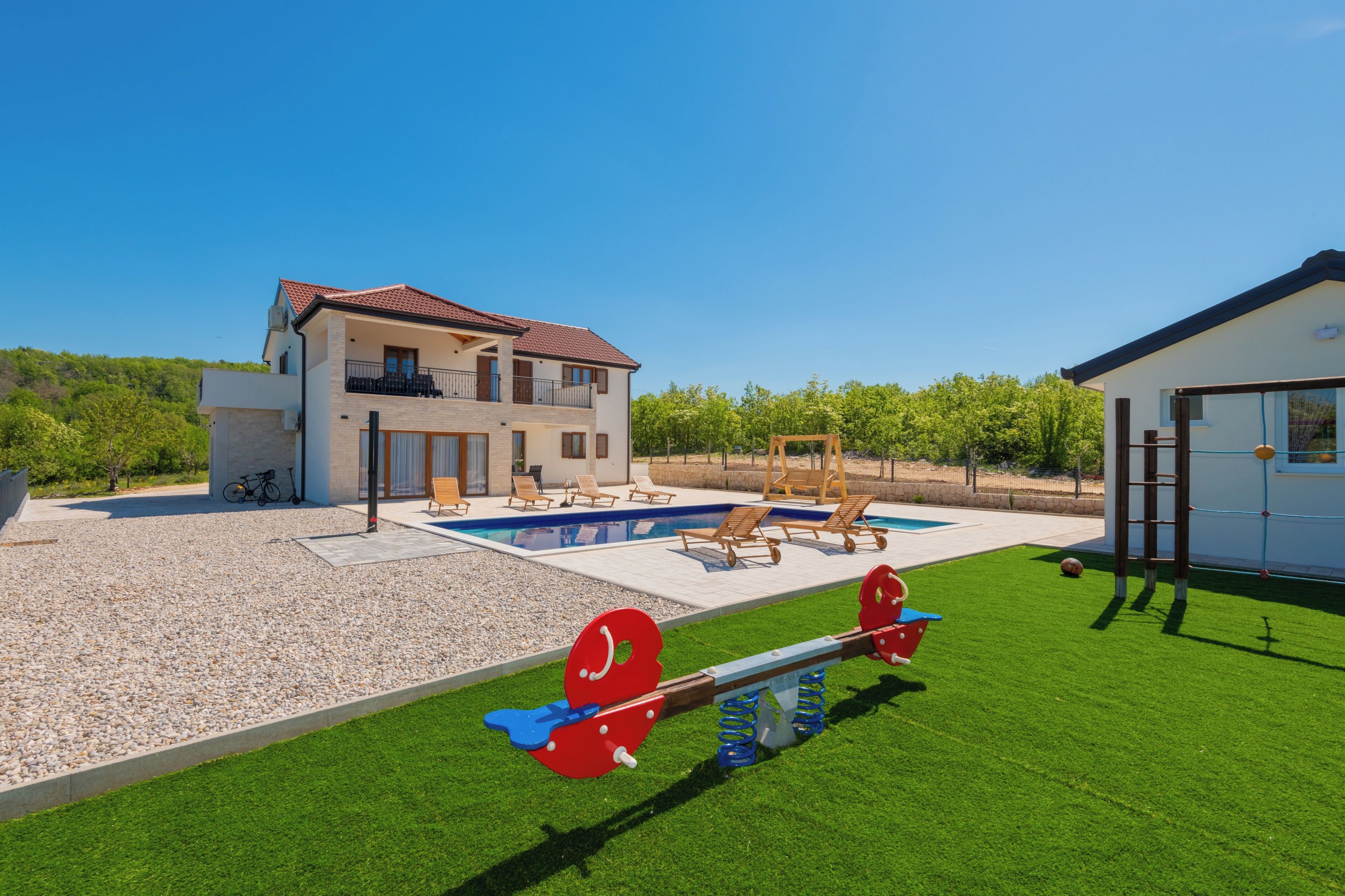 A modern two-story house with a swimming pool, outdoor seating, and a seesaw.