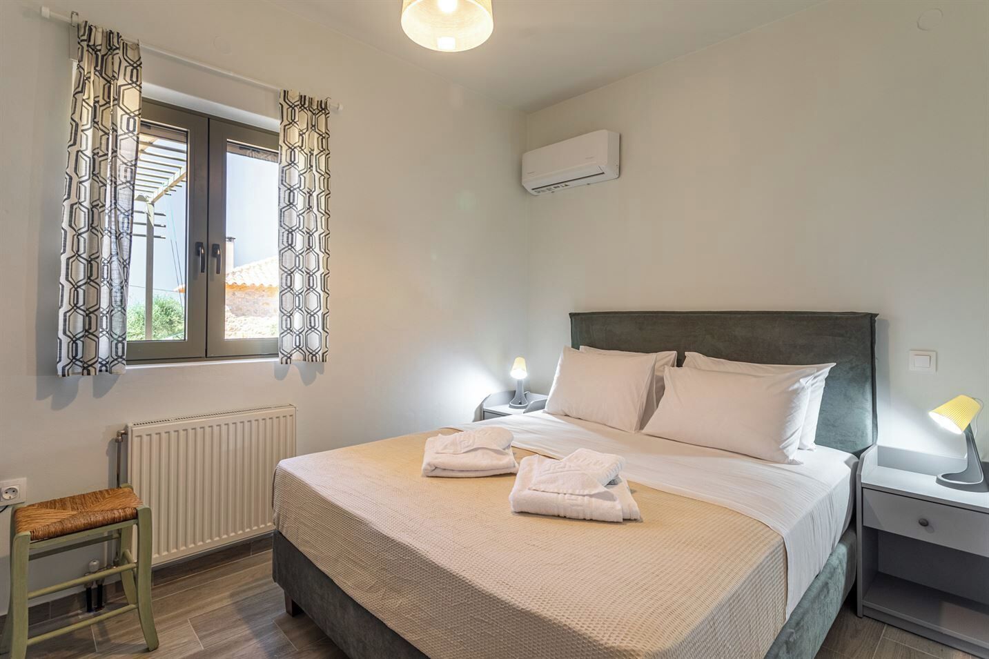 Una camera da letto ordinata con un letto, due lampade da comodino, un termosifone e una finestra con tende a motivi.