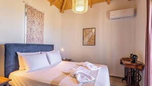 A bedroom with a large bed, a wooden headboard, a bedside table with a lamp, an air conditioning unit, and a sewing machine on a wooden table.