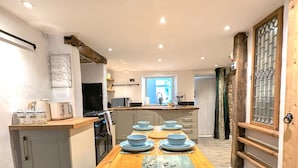 Una cocina moderna con una mesa de madera dispuesta para seis comensales, horno empotrado y ventana con cortinas.