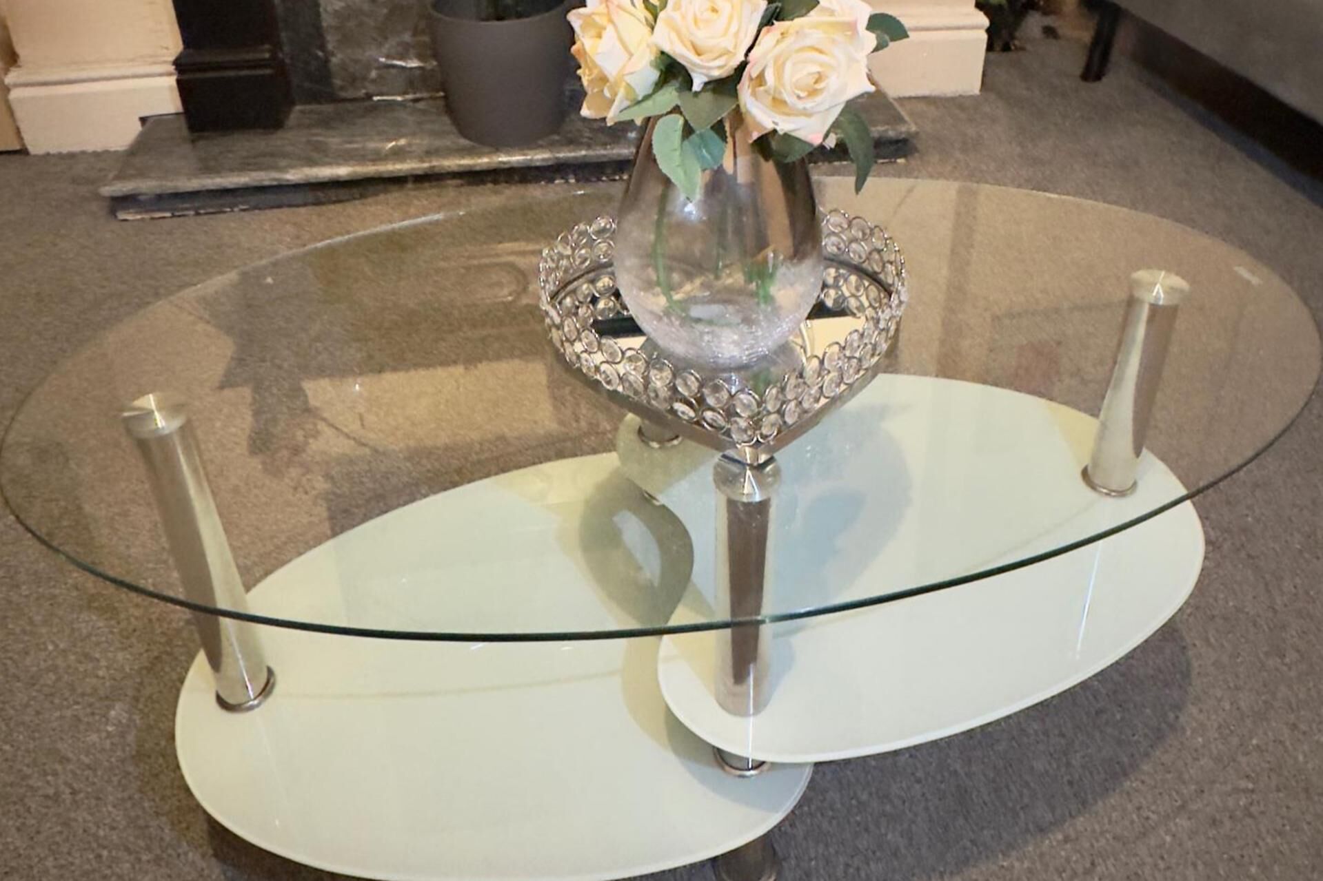 Un tavolo con piano in vetro, un vaso di fiori e una base decorativa.