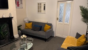 A living room with a grey sofa, yellow cushions, a glass coffee table, and a white door with decorative glass panels. - Cozy Accrington Retreat (Accrington)