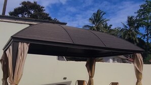 An outdoor patio with a covered seating area, stone flooring, and potted plants. - GL Homez (Tanga)
