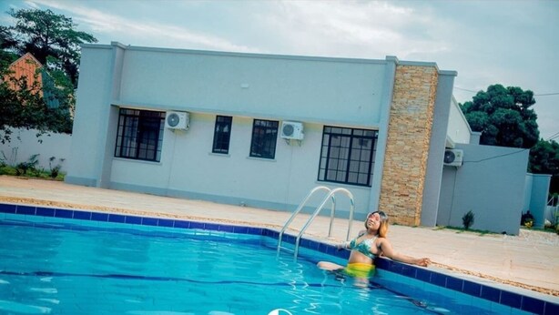 A swimming pool with a person in the water, a modern building with windows and air conditioning units, and a logo 'GL HOMEZ' at the bottom. - GL Homez (Tanga)